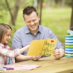 Daughter shows dad handmade Father’s Day card. Outdoors. Child, parent.